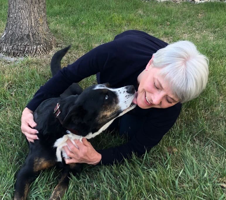 A person with long curly hair sitting at a table with laptop, notepads and latte in a clear glass cup.