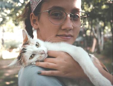 Young woman with white cat with different brown or grey colours on its head and back.